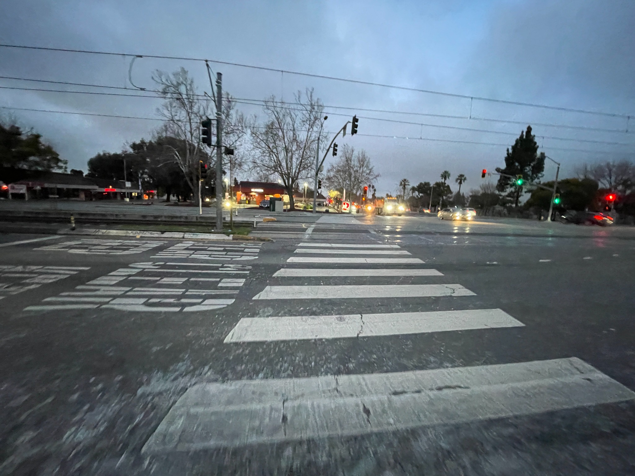 Evening view of a wide crosswalk near rail with traffic lights and cars