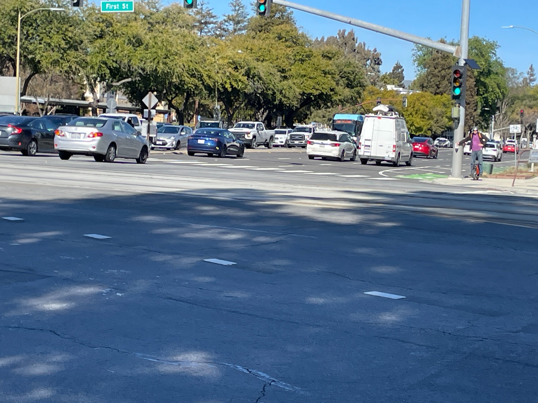 Busy daylight intersection with vehicles and a person on a scooter near tracks